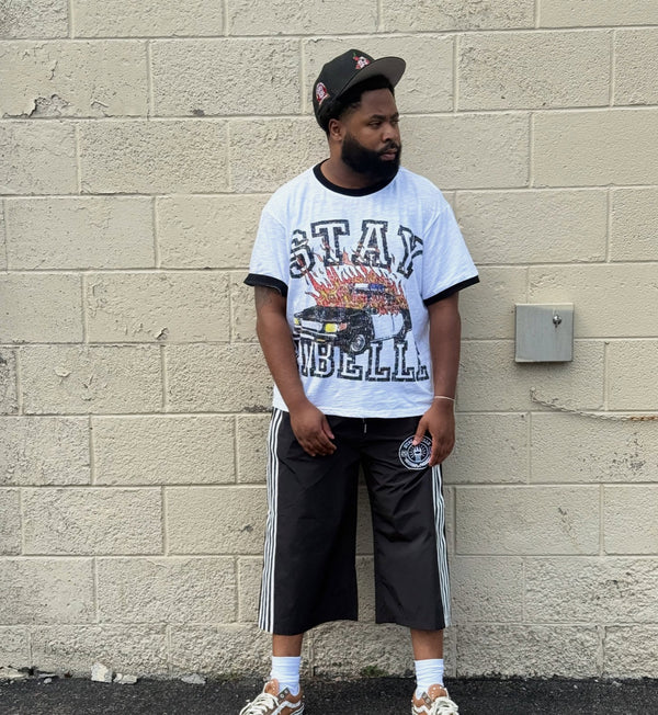 Customer in a white Stay Ribelle graphic tee and black track shorts against a cinder-block wall