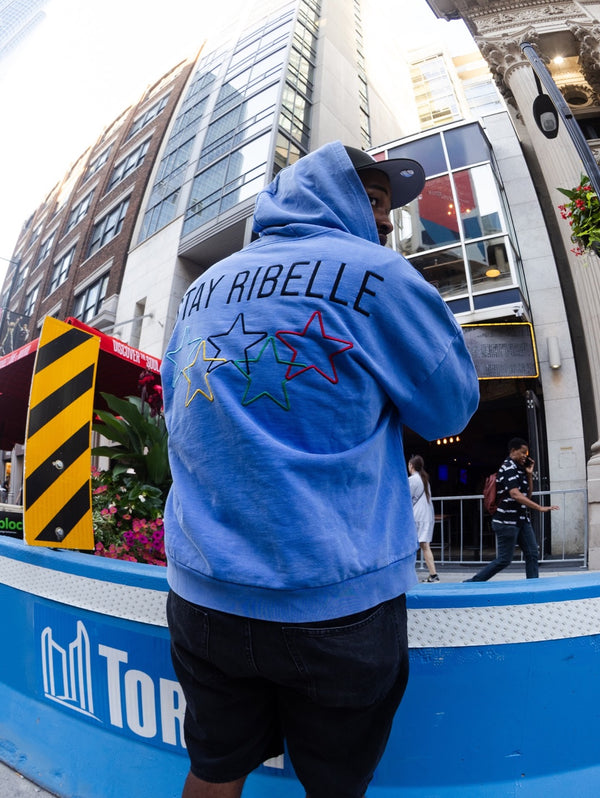 Back view of a periwinkle Stay Ribelle star hoodie on a city street