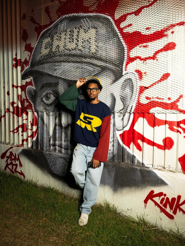 Customer in a navy, red and green Stay Ribelle logo sweater in front of a graffiti mural
