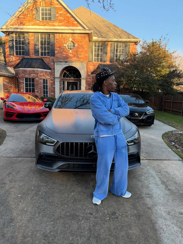 Customer in a light-blue Stay Ribelle sweatsuit beside a car in a driveway