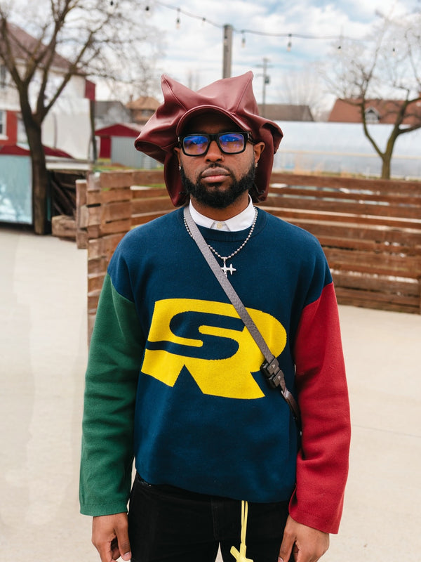 Customer in a green, navy and red Stay Ribelle logo sweater and a red bucket hat