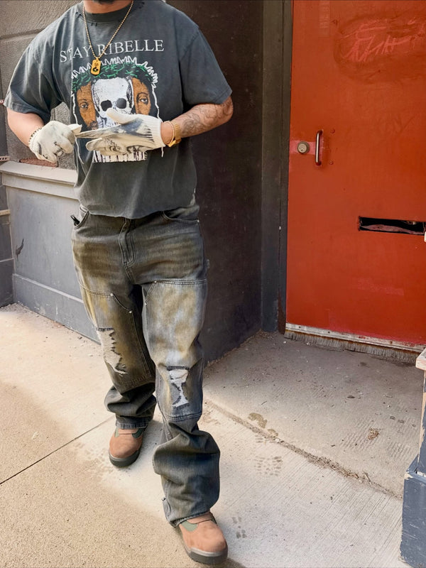 Customer in a charcoal Stay Ribelle graphic tee and distressed jeans by an orange door